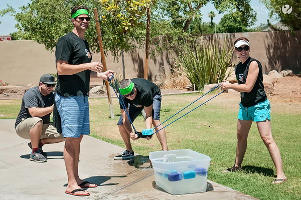 Sponge Launch. Three team members use the water balloon launch to launch sponges filled with water to their team mates. Teammates catch the sponges and wring the sponge out in the bucket. Once the bucket is full, you win the game.