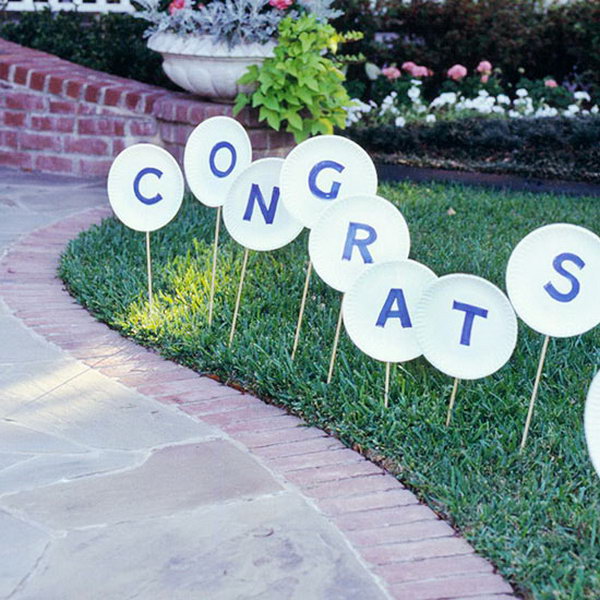 Wooden Sign Graduation Party. Direct your guests with this wooden sign to your front walk. Cut letters from blue paper and glue to paper plates. Attach wonder dowels and stick into the lawn for simple graduation party decor without costing too much.