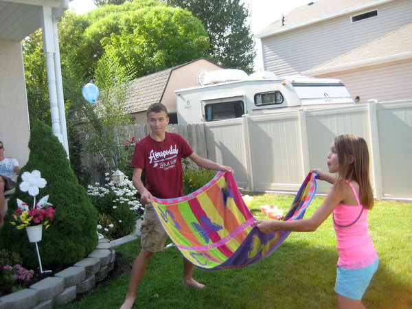 Water Balloon Towel Toss. Group the team members, put the water balloon in the center and toss it using snapping motion and the other team should try to catch it. You can have extra challenge by taking a step back if you catch it. It's really a challenging game for kids to have fun.